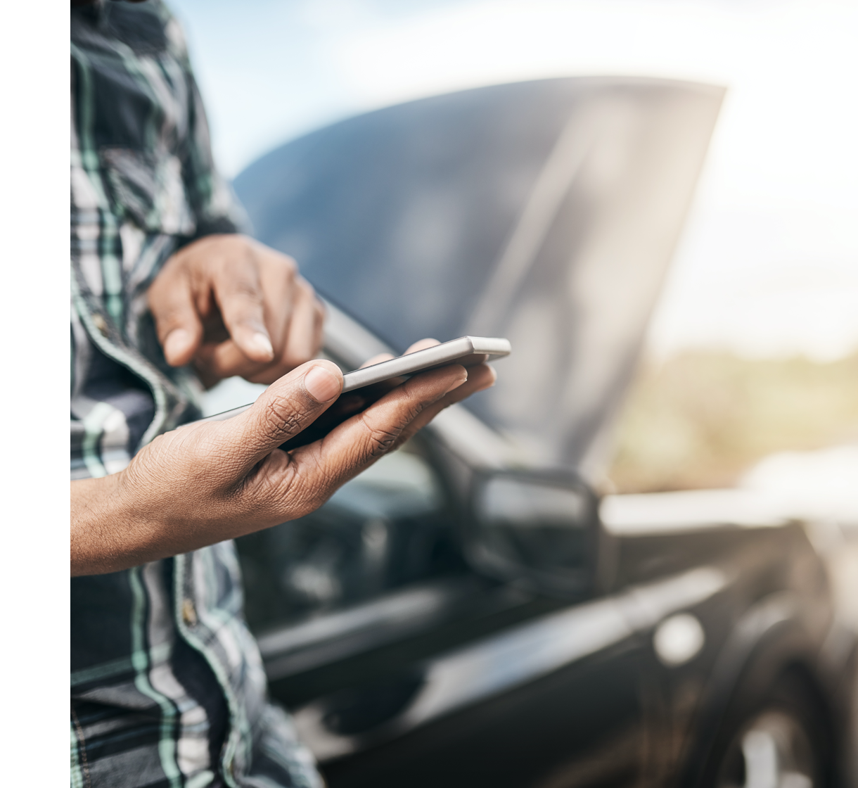 Persona usa uno smartphone davanti a un’auto in panne con il cofano aperto.